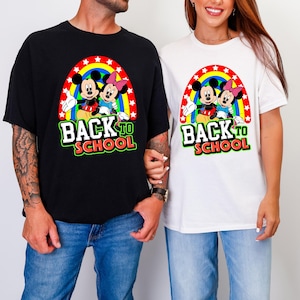 Puede incluir: Camisetas negras y blancas con un gráfico colorido de Mickey y Minnie Mouse bajo un arcoíris con estrellas. El texto "BACK TO SCHOOL" se muestra en verde y blanco. Las camisetas son usadas por dos personas.