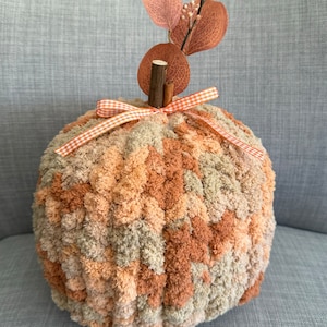 May include: A brown and beige yarn pumpkin with a gingham ribbon and a brown twig with dried leaves on top.