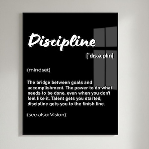 May include: A black framed wall art print with the word "Discipline" in white script. The definition of discipline is provided below the word, along with its pronunciation and the phrase "(see also: Vision)." The print is displayed on a white brick wall.