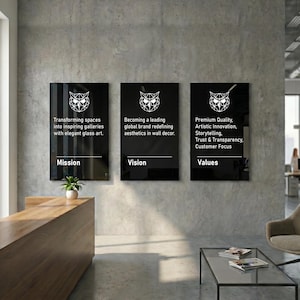 Op de afbeelding: Drie zwarte rechthoekige borden met witte tekst en een geometrisch uil-logo zijn bevestigd aan een grijze betonnen muur. De borden luiden "Missie", "Visie" en "Waarden", met beschrijvende tekst eronder. Moderne kantooromgeving.