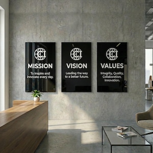 Puede incluir: Tres letreros negros enmarcados con texto blanco y un logotipo están montados en una pared de hormigón gris. Los letreros dicen "MISIÓN", "VISIÓN" y "VALORES", con texto de apoyo debajo. Una pequeña planta se encuentra en un mostrador de madera.