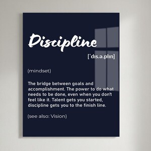 May include: A black framed wall art print with the word "Discipline" in white script. The definition of discipline is provided below the word, along with its pronunciation and the phrase "(see also: Vision)." The print is displayed on a white brick wall.