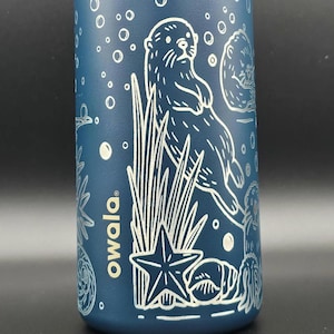 May include: A blue water bottle featuring a white illustration of an otter, seaweed, starfish, and bubbles. The word "owala" is printed in white. The bottle is designed for hydration and outdoor activities.