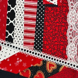 May include: A patchwork quilt made of red, black, and white fabric with a variety of patterns, including hearts, polka dots, and stripes. The quilt is edged with white lace.