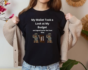 May include: Black t-shirt with a humorous saying about a wallet taking a look at a budget. The text reads "My Wallet Took a Look at My Budget and signed up for the front lines". Two cartoon dogs wearing military hats and holding a "Private Wallet" sign are on either side of the text.