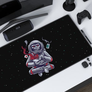 Puede incluir: Un tapete de ratón para juegos negro con un diseño de mono astronauta blanco. El mono está sentado en una postura meditativa y sostiene un tazón de ramen. El fondo es un espacio negro con estrellas blancas.