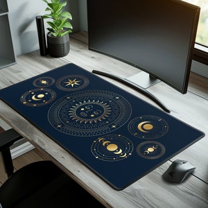 May include: A navy blue desk mat featuring a celestial design with gold sun, moon, and star illustrations. The mat is rectangular and sits on a wooden desk, next to a computer monitor and mouse.