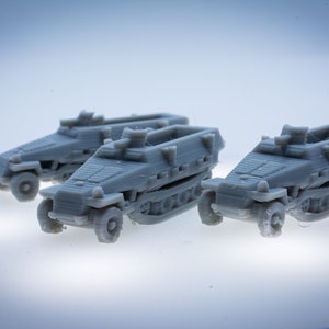 Può includere: Tre veicoli militari grigi in miniatura con cingoli e ruote sono disposti su una superficie bianca. I veicoli hanno un design squadrato con dettagli, tra cui un frontale inclinato e una piccola struttura a forma di torretta.