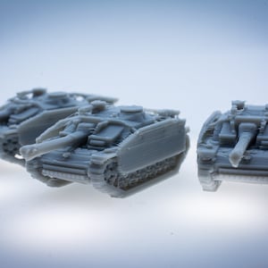 以下が含まれることがあります： グレーのミニチュア戦車3台。砲塔、大砲、キャタピラなどの詳細な特徴があります。戦車は明るい表面に配置され、そのデザインと構造を示しています。画像はモデルの複雑な詳細を強調しています。