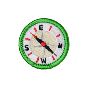 May include: Embroidered compass patch with a green border. The compass rose features a beige center, black and red needle, and directional markings (N, S, E, W). The patch is round and has a white background.