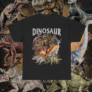 Puede incluir: Camiseta negra con un estampado gráfico de varios dinosaurios, incluyendo un Tyrannosaurus Rex, un Triceratops y un Stegosaurus. El texto "DINOSAUR" está impreso en blanco sobre los dinosaurios.