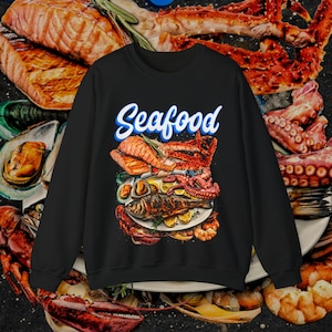 May include: Black sweatshirt featuring a graphic design of a seafood platter. The platter includes grilled salmon, prawns, octopus, and a whole fish. The text "Seafood" is written in blue and white lettering on the sweatshirt.
