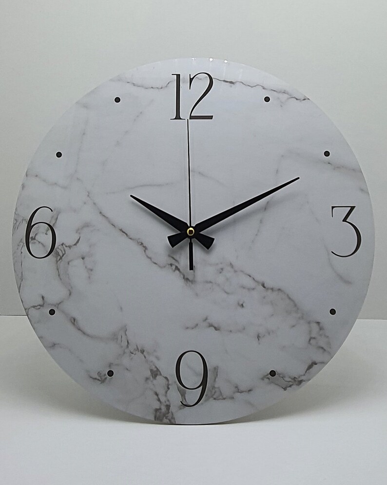May include: White round clock with black hands and black numbers on a marble-patterned face. The numbers 12, 6, 3, and 9 are visible.