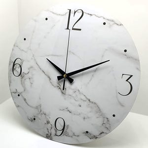 May include: A white round clock with black hands and black numbers on a marble-patterned background. The numbers 12, 3, 6, and 9 are visible.