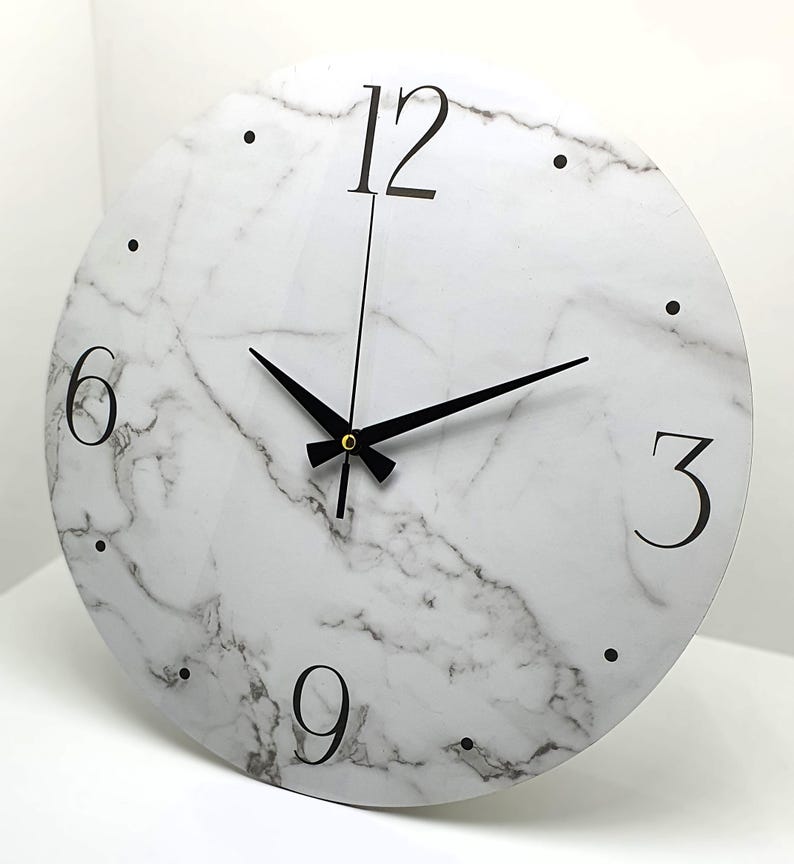 May include: A white round clock with black hands and black numbers on a marble-patterned background. The numbers 12, 3, 6, and 9 are visible.