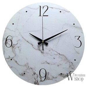 May include: White round wall clock with black hands and black Roman numeral markings on a white marble background. The clock face has a subtle gray marble pattern. The clock is 12 inches in diameter.
