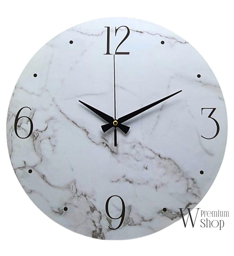 May include: White round wall clock with black hands and black Roman numeral markings on a white marble background. The clock face has a subtle gray marble pattern. The clock is 12 inches in diameter.