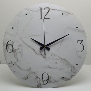 May include: A white round clock with black hands and black numbers on a marble-patterned face. The numbers 12, 6, 3, and 9 are visible.