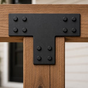 May include: A matte black T-shaped metal plate connector secured to two intersecting wooden beams. The bracket features twelve hexagonal bolt heads arranged in a symmetrical pattern, providing a structural connection between the horizontal and vertical timber pieces.