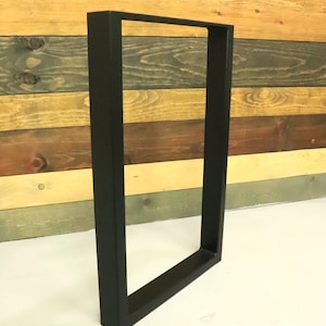 Op de afbeelding: Zwarte metalen tafelpoten met een rechthoekig frame. De poten staan op een wit oppervlak.