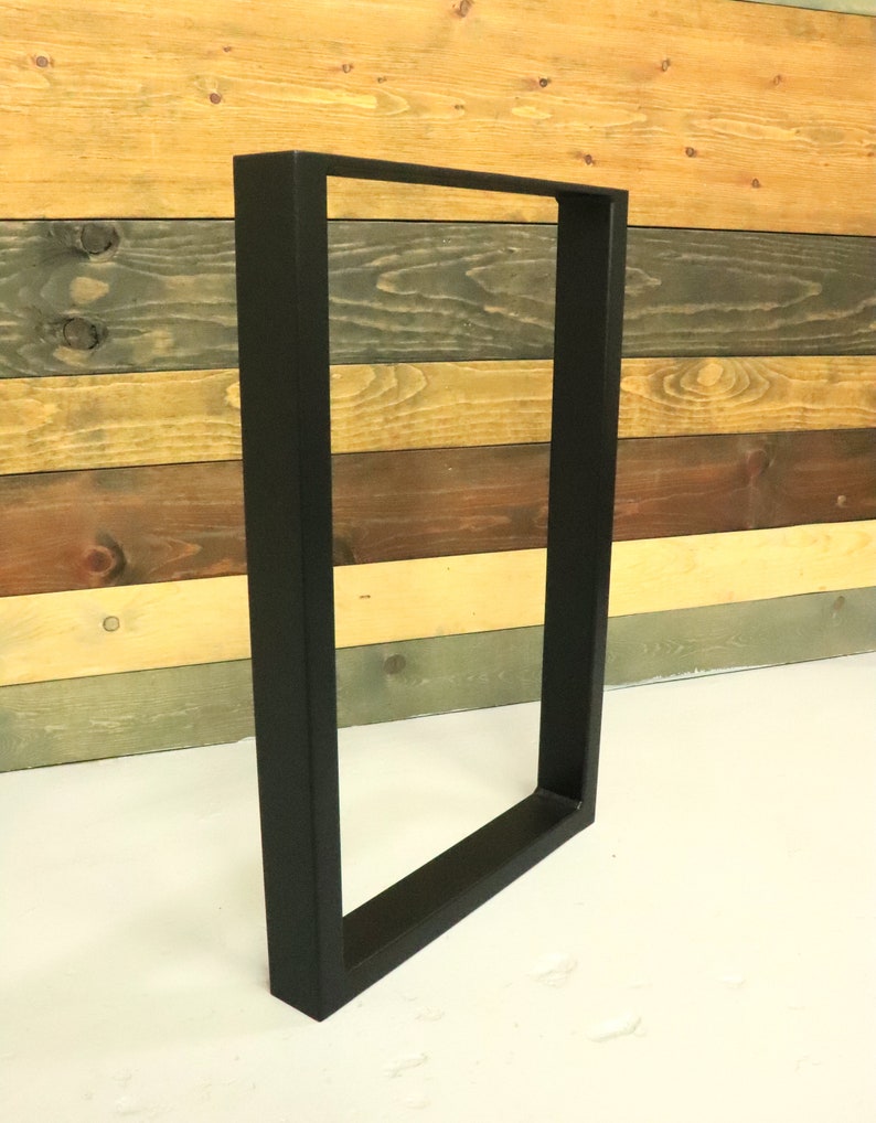 Op de afbeelding: Zwarte metalen tafelpoten met een rechthoekig frame. De poten staan op een wit oppervlak.