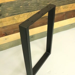 Op de afbeelding: Zwart metalen tafelpoot met een rechthoekig frame. De poot is gemaakt van dik metaal en heeft een matte zwarte afwerking.