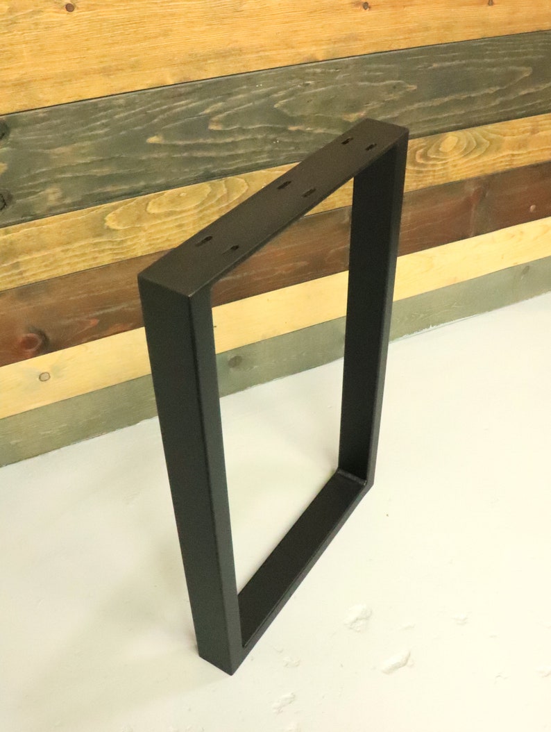 Op de afbeelding: Zwart metalen tafelpoot met een rechthoekig frame. De poot is gemaakt van dik metaal en heeft een matte zwarte afwerking.