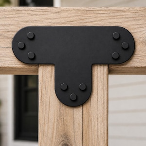 May include: A matte black metal T-shaped structural connector plate secured with six matching hexagonal bolts, mounted onto light brown wooden beams. The hardware features rounded edges and a smooth finish, providing a stable joint connection.