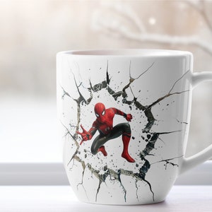 Puede incluir: Taza de cer&aacute;mica blanca con un gr&aacute;fico de Spider-Man rompiendo una pared agrietada. La taza tiene un asa negra.