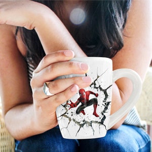 Puede incluir: Taza de cer&aacute;mica blanca con un dise&ntilde;o agrietado que presenta un personaje de Spiderman rojo y azul. La taza tiene un asa.