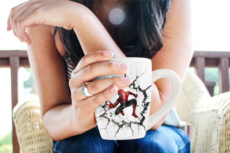 Puede incluir: Taza de cer&aacute;mica blanca con un dise&ntilde;o agrietado que presenta un personaje de Spiderman rojo y azul. La taza tiene un asa.