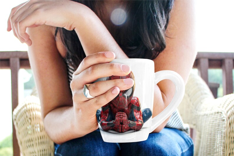 K&ouml;nnte beinhalten: Wei&szlig;e Keramik-Tasse mit detailliertem Bild von Spider-Man in meditativer Pose. Der Superheld ist in seinem klassischen rot-schwarzen Anzug dargestellt, die H&auml;nde gefaltet. Die Tasse hat einen gebogenen Henkel.