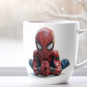 K&ouml;nnte beinhalten: Wei&szlig;e Keramiktasse mit einer detaillierten Illustration von Spider-Man in einer sitzenden, meditativen Pose. Der Superheld ist in seinem klassischen rot-blauen Anzug dargestellt, die H&auml;nde gefaltet. Die Tasse hat einen gebogenen Griff.