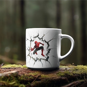 Puede incluir: Taza de cer&aacute;mica blanca con un gr&aacute;fico de Spiderman rompiendo una pared agrietada. La taza tiene un asa negra.
