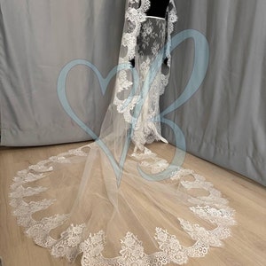 May include: A white bridal veil with a delicate lace trim. The veil is long and flowing, with a scalloped edge. The lace is intricate and detailed, with a floral pattern.
