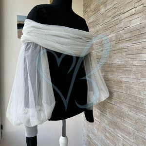 May include: A white tulle off-the-shoulder top with long, puffy sleeves. The top is on a black mannequin.