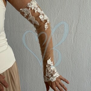 May include: White lace elbow-length gloves with floral embroidery on a sheer mesh fabric.