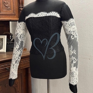 May include: A black lace top with long sleeves and a white lace trim. The sleeves are sheer and have a delicate floral pattern.