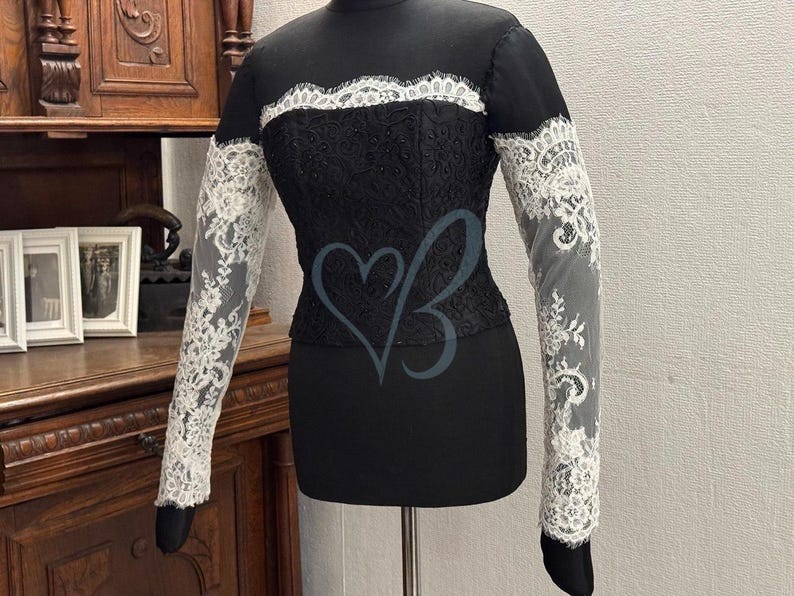 May include: A black lace top with long sleeves and a white lace trim. The sleeves are sheer and have a delicate floral pattern.