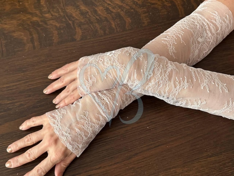 May include: Delicate white lace arm warmers with a floral pattern. The arm warmers are made of a sheer, lightweight fabric. The lace design adds a touch of elegance. Perfect for weddings, parties, or special occasions.