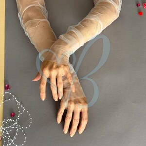K&ouml;nnte beinhalten: Ein Paar wei&szlig;e, durchsichtige Ellbogenhandschuhe. Die Handschuhe sind aus einem zarten, leichten Stoff gefertigt und haben einen leicht gerafften Look.