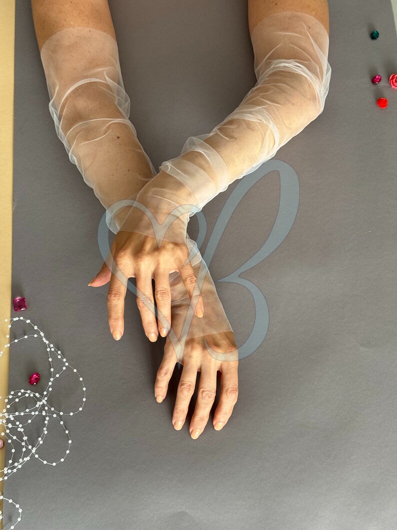 K&ouml;nnte beinhalten: Ein Paar wei&szlig;e, durchsichtige Ellbogenhandschuhe. Die Handschuhe sind aus einem zarten, leichten Stoff gefertigt und haben einen leicht gerafften Look.