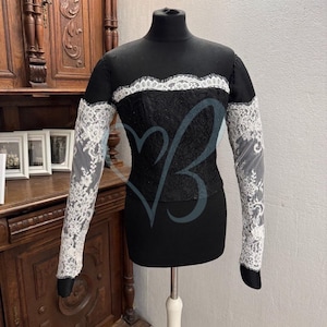 May include: A black long-sleeved top with a white lace trim around the neckline and on the sleeves. The top is made of a stretchy fabric and has a fitted silhouette.