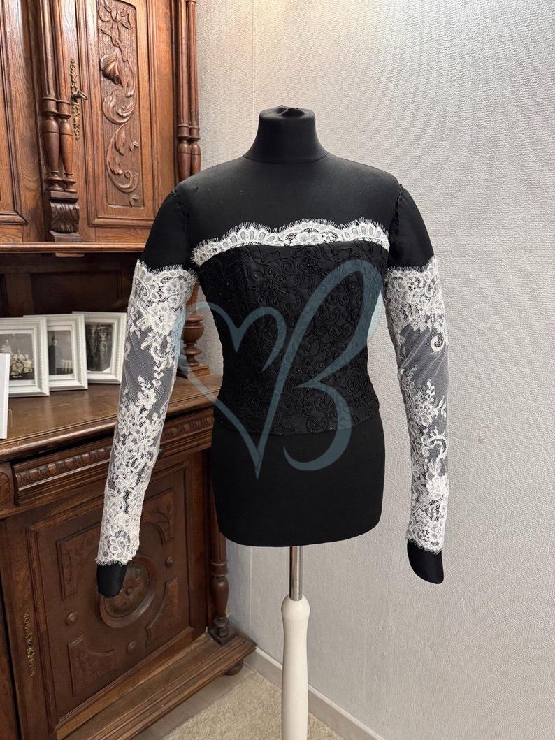 May include: A black long-sleeved top with a white lace trim around the neckline and on the sleeves. The top is made of a stretchy fabric and has a fitted silhouette.