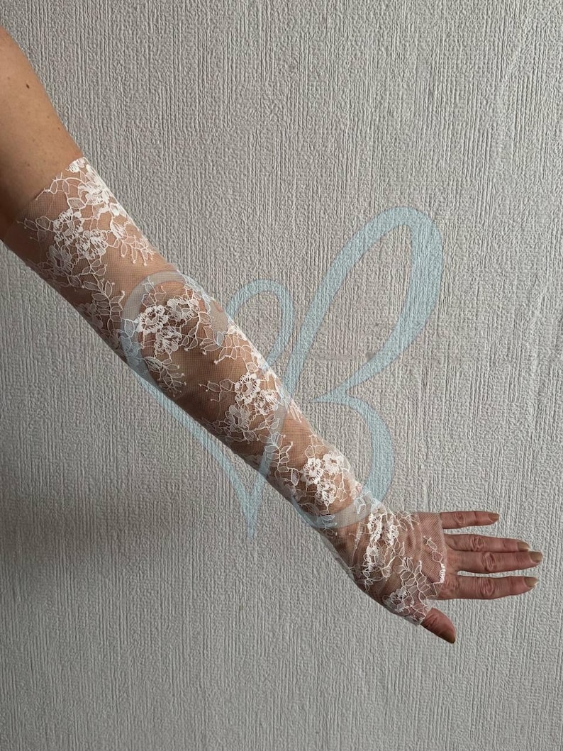 K&ouml;nnte beinhalten: Wei&szlig;e Spitzengloves mit floralem Muster. Die Handschuhe reichen von den Fingerspitzen bis zum Oberarm. Die Spitze ist detailliert und zart, wodurch ein romantischer und eleganter Look entsteht. Perfekt f&uuml;r Hochzeiten oder besondere Anl&auml;sse.