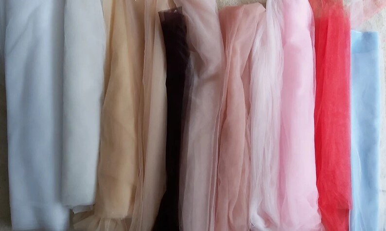 K&ouml;nnte beinhalten: Sortiment von zehn durchsichtigen Stoffproben in verschiedenen Farben, darunter Wei&szlig;, Beige, Braun, Rosa, Hellrosa, Rot und Blau.