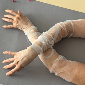 K&ouml;nnte beinhalten: Ein Paar wei&szlig;e, durchsichtige Ellbogenhandschuhe. Die Handschuhe sind aus einem zarten, leichten Stoff gefertigt und perfekt, um jedem Outfit einen Hauch von Eleganz zu verleihen.