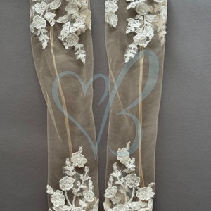 May include: A pair of sheer white lace gloves with floral embroidery. The gloves are made of a delicate fabric and have a soft, feminine look.