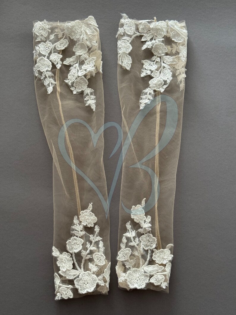 May include: A pair of sheer white lace gloves with floral embroidery. The gloves are made of a delicate fabric and have a soft, feminine look.