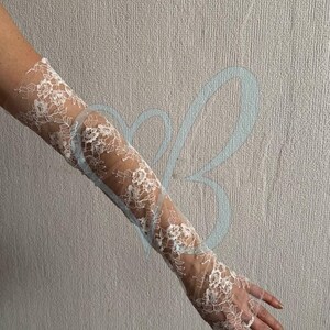 K&ouml;nnte beinhalten: Wei&szlig;e Spitzenhandschuhe mit floralen Mustern. Die Handschuhe sind lang und reichen bis zum Arm. Das filigrane Spitzendesign ist sichtbar und erzeugt einen eleganten, romantischen Look. Die Handschuhe sind wahrscheinlich f&uuml;r einen besonderen Anlass.